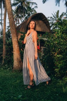 Portrait of beautiful lady in white striped dress with balinese vila background. Young model girl posing in tropical jungle nature