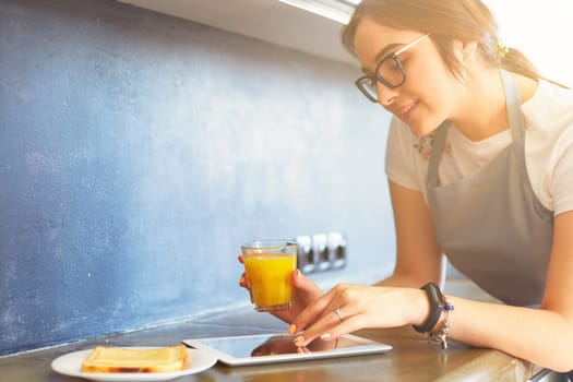 Portrait of young attractive caucasian brunette housewife at kitchen. Morning with cup of coffee and tablet pc.