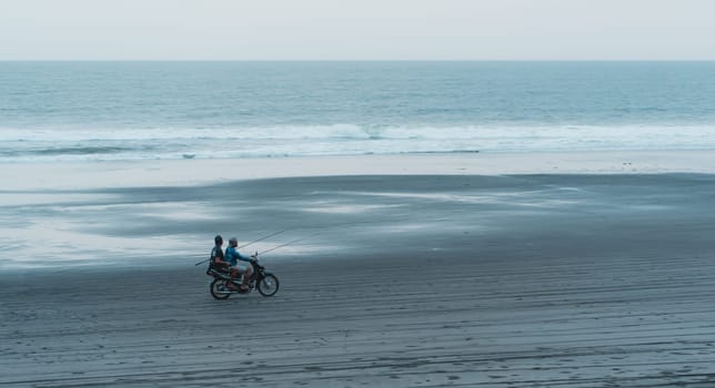 Landscape view of two bikers driving on beach with sea background. Riding a scooter on the ocean sand