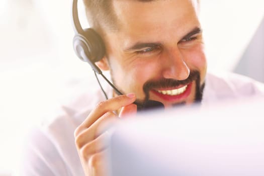 Portrait of a young man with a headset in front of a laptop computer.