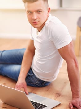 Attractive young man lying on wooden floor and using laptop.