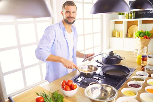 Man following recipe on digital tablet and cooking tasty and healthy food in kitchen at home.