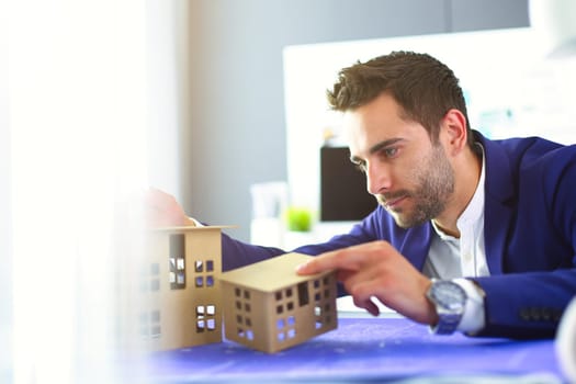 Businessman holding house miniature on hand standing in office