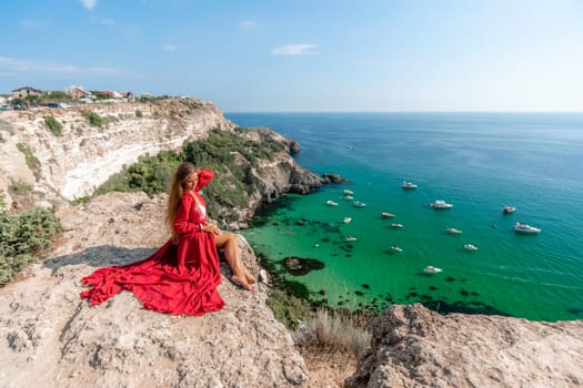 Woman red dress sea. Happy woman in a red dress and white bikini sitting on a rocky outcrop, gazing out at the sea with boats and yachts in the background