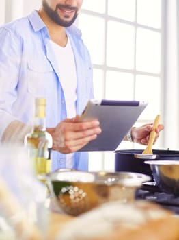 Man following recipe on digital tablet and cooking tasty and healthy food in kitchen at home.