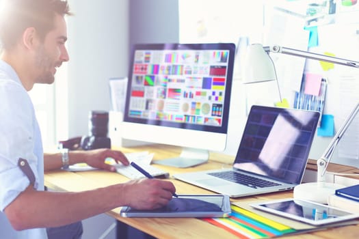 Portrait of young designer sitting at graphic studio in front of laptop and computer while working online