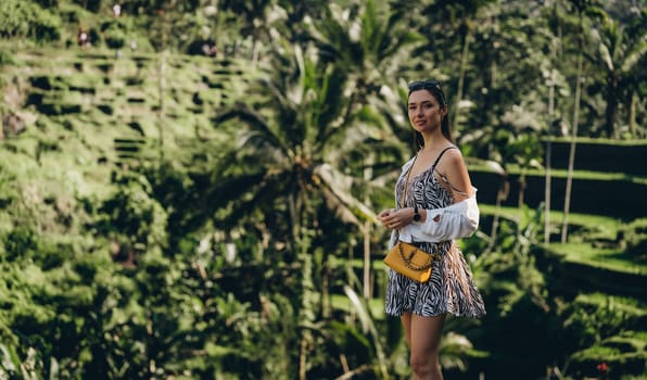 Close up shot of beautiful girl standing on rice terrace with green nature background. Young lady in summer outfit admiring balinese paddy fields