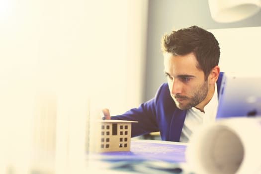 Businessman holding house miniature on hand standing in office