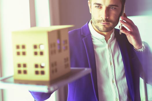 Businessman holding house miniature on hand standing in office