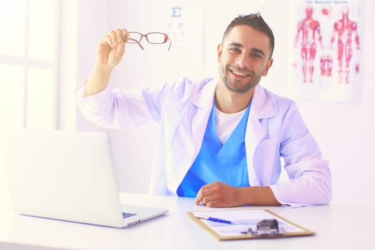 Portrait of a male doctor with laptop sitting at desk in medical office