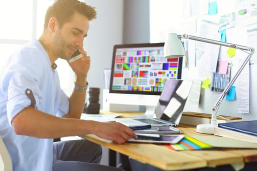 Portrait of young designer sitting at graphic studio in front of laptop and computer while working online