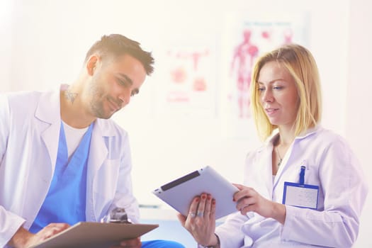 Handsome doctor is talking with young female doctor and making notes while sitting in his office