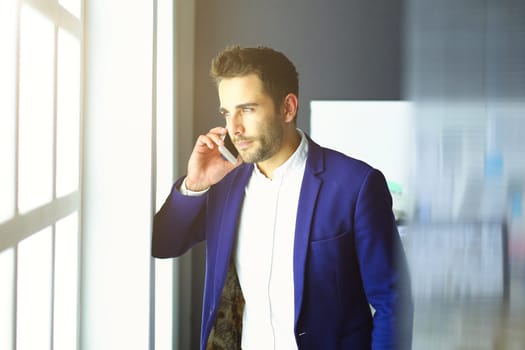 Business man in suit talking on phone and looking away near the window