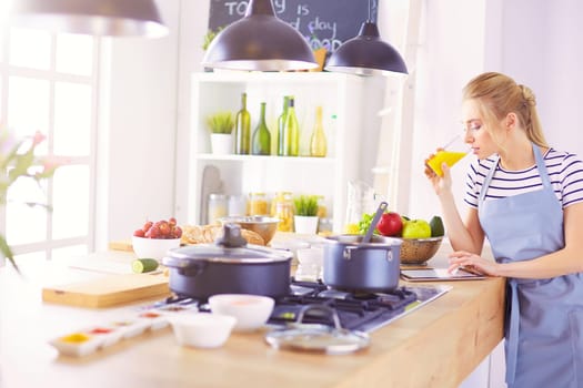 Attractive woman holding a glass of orange juice while standing in the kitchen.