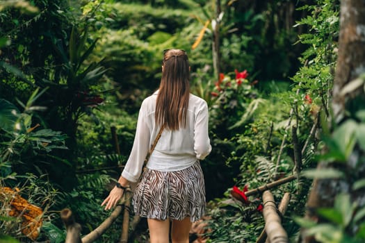 Back view of walking beautiful lady through jungle vegetation. Young girl exploring beauty of tropical nature