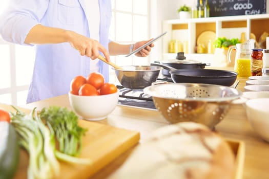 Man following recipe on digital tablet and cooking tasty and healthy food in kitchen at home.