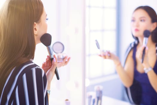 Beautiful girl looking in the mirror and applying cosmetic with a big brush.