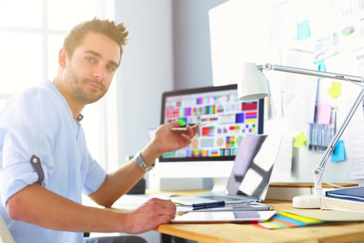 Portrait of young designer sitting at graphic studio in front of laptop and computer while working online