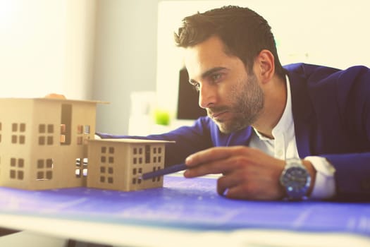 Businessman holding house miniature on hand standing in office