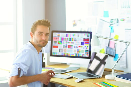 Portrait of young designer sitting at graphic studio in front of laptop and computer while working online