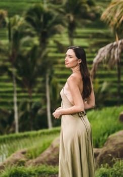 Stylish lady in green sexy dress on footpath rice terrace. Young elegant lady admiring evergreen balinese nature