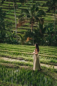 Beautiful girl in green dress walking on rice terrace. Elegant lady visiting rice plantation