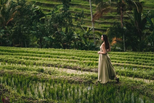 Beautiful girl in green dress walking on rice terrace. Elegant lady visiting rice plantation