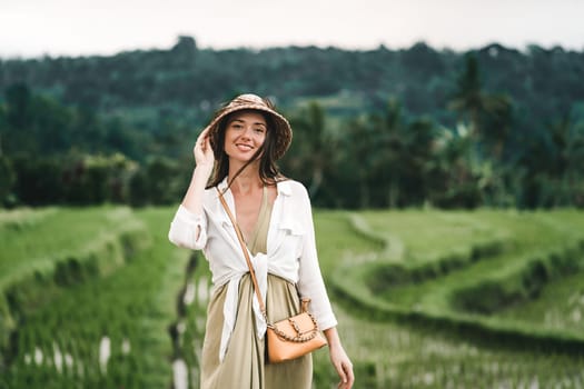 Close up shot of beautiful girl with traditional balinese hat on rice terrace background. Smiling lady in paddy field