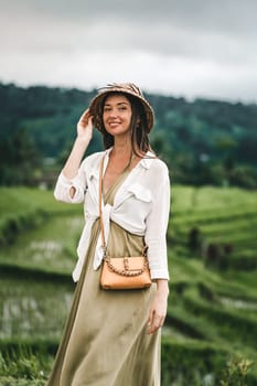 Portrait of happy girl with balinese hat on rice terrace. Excited girl looking around balinese rice plantation