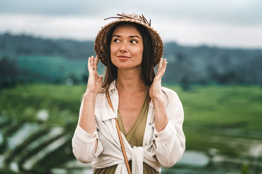 Close up shot of beautiful girl with traditional balinese hat on rice terrace background. Smiling lady in paddy field