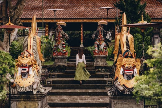 Girl climbing stairs decorated with traditional barong statues. Balinese culture and decorative architecture