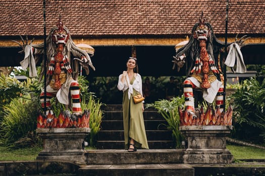 Beautiful girl between two statues with barong mask. Religious hindu ritual temple with colorful sculptures