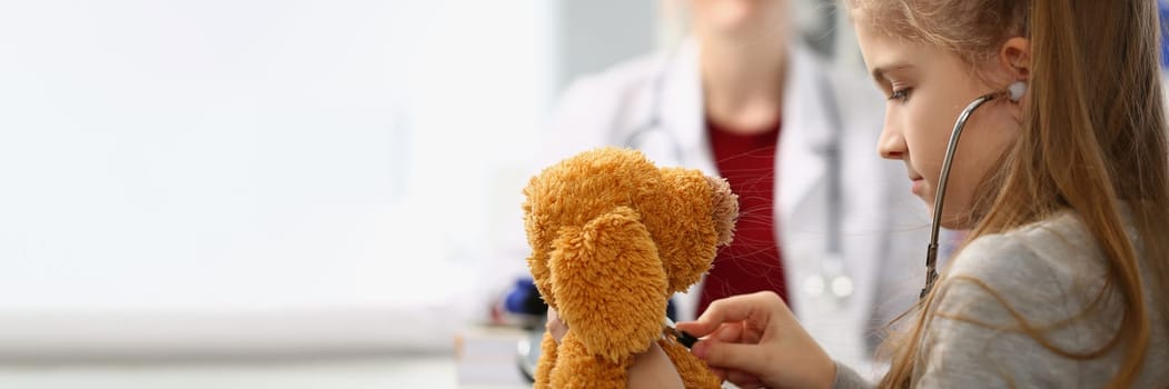 Girl child with stethoscope listens to toy in background sits doctor. Children medicine pediatrics and insurance