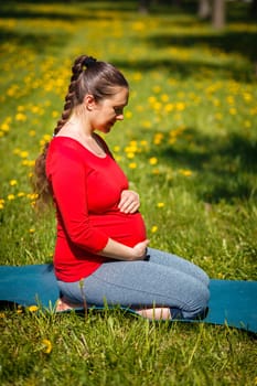 Pregnancy yoga exercise - pregnant woman doing asana Virasana Hero Pose on knees outdoors on grass lawn with dandelions in summer