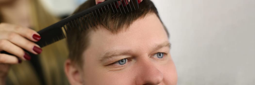 Hairdresser cuts hair with scissors and black comb. Satisfied client man sitting in barbershop salon