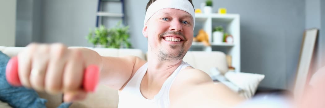 Emotional happy excited young man posing with dumbbells and taking selfie. Athlete man doing exercises with dumbbells at home