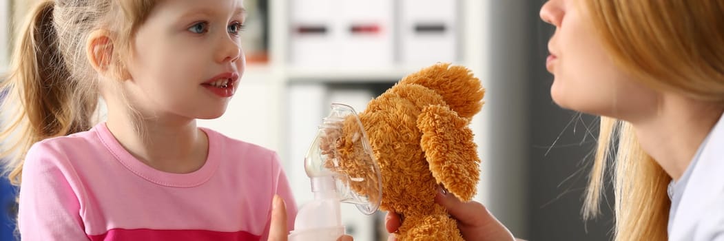 Pediatrician shows little girl on toy how to use oxygen mask. Treatment of asthma, pneumonia and bronchitis in children