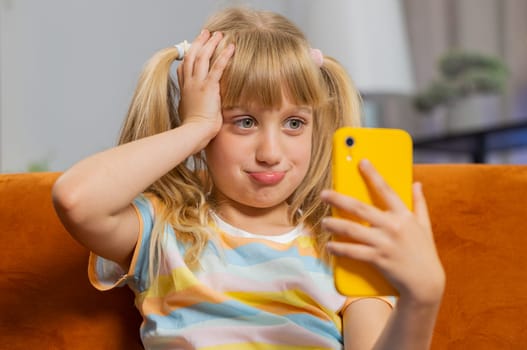Child kid girl use smartphone, playing game, loses becoming surprised sudden lottery results, bad news, fortune loss, fail education study test. Female teen toddler at home in living room sits on sofa