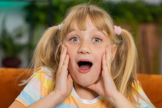 Oh my God, Wow. Caucasian surprised preteen school girl looking at camera with big eyes, shocked by sudden victory, good win news, celebrating. Excited amazed child kid at home room sitting on couch