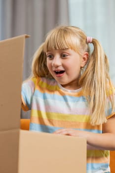 Happy child kid girl unpacking delivery parcel. Smiling satisfied teen toddler shopper online shop customer opening cardboard box receiving purchase gift by fast postal shipping at home. Vertical shot