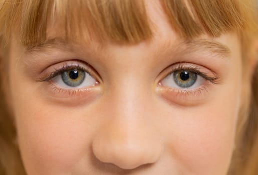 Extreme close-up macro portrait of smiling girl face. Teen beautiful kid's eyes looking at camera. Young positive toddler child opening wide her closed eyes. Gray eyes of blonde female children model