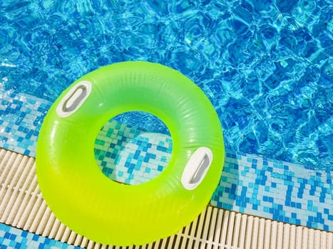 Bright inflatable tube ring floating on blue water surface with splashes in swimming pool during daytime