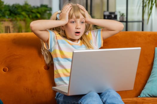 Portrait of caucasian toddler girl use laptop typing browsing working, loses becoming surprised sudden lottery results, bad news, fortune loss, fail. Teen child kid at home in play room on couch