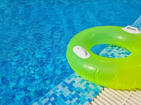 Bright inflatable tube ring floating on blue water surface with splashes in swimming pool during daytime
