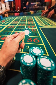 Casino, gambling and entertainment concept - male hand with stack of poker chips on a green table background