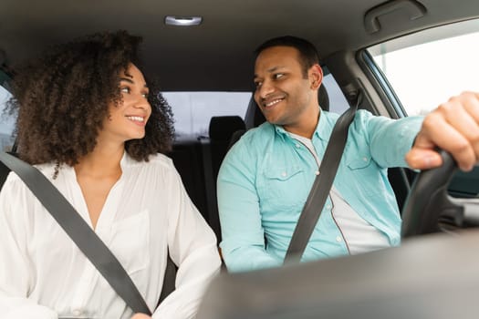 Car Travel. Smiling young arabic couple man and woman posing in car with fastened safety seat belts, looking at each other. Joyful spouses having trip by comfy luxury auto, view from dashboard