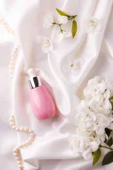 A jar of liquid cream with flowers on a white flowing satin.