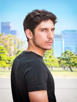 Head and shoulders shot of one handsome young man with green eyes in urban setting, looking at camera, wearing t-shirt