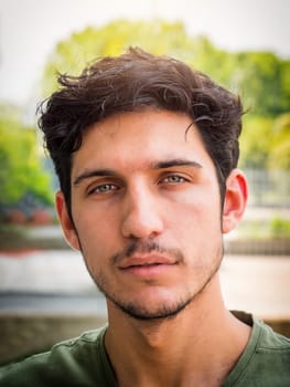 Head and shoulders shot of one handsome young man with green eyes in urban setting, looking at camera, wearing t-shirt