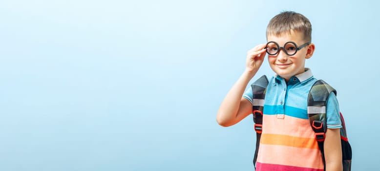 Positive elementary school nerd boy in eyeglasses against blue background.